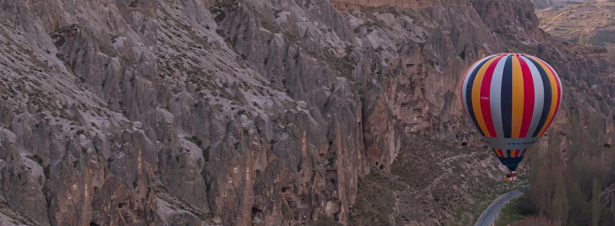 A hot air balloon flying beside the rock-cut cliffs of Soganli Valley in Cappadocia